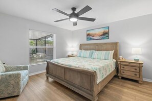 Une chambre à coucher avec un lit en bois, deux tables de chevet, un ventilateur de plafond et une fenêtre avec des stores.