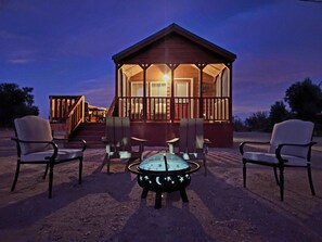A wooden cabin with a porch, four chairs, and a fire pit. - Dark Sky Cabin on 10 Acres Near Death Valley (Amargosa Valley)