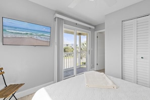 Ein Schlafzimmer mit Bett, Fernseher an der Wand und einer Glastür zum Balkon mit Meerblick.