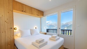 Ein Schlafzimmer mit Holz-Kopfteil, einem großen Bett mit weißer Bettwäsche, zwei Nachttischlampen und Bergblick durch ein Fenster.