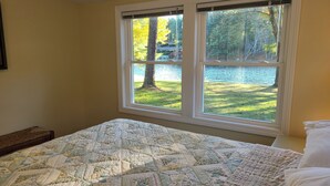 Une chambre avec une grande fenêtre donnant sur un lac et des arbres.