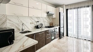 A modern kitchen with marble countertops, a built-in oven, and a large window with sheer curtains.