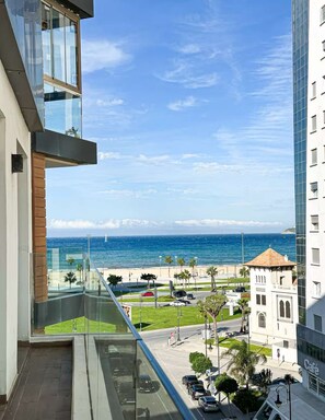 Un immeuble de grande hauteur doté d’un balcon donnant sur une plage et sur un café.