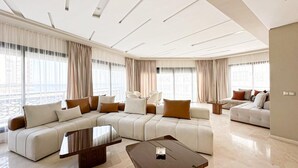 A spacious living room with a sectional sofa, a coffee table, and a view of the city through large windows.