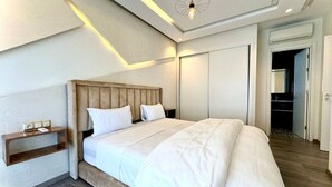 A modern bedroom with a large bed, wooden headboard, bedside tables, and a ceiling light fixture.