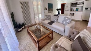 Un salon moderne avec une table basse en verre, un canapé et un coin repas, avec une cuisine en arrière-plan.
