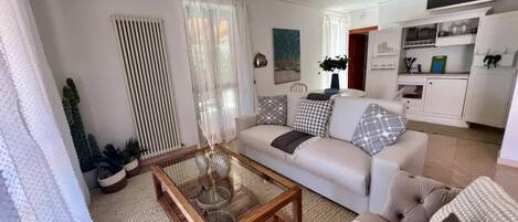 Un salon moderne avec une table basse en verre, un canapé et un coin repas, avec une cuisine en arrière-plan.