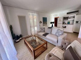 Una sala de estar moderna con una mesa de centro de vidrio, un sofá y un comedor con una cocina al fondo.
