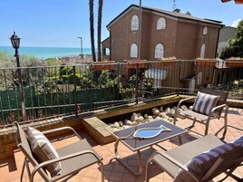 Una terraza con mobiliario exterior, vista al mar y un edificio de ladrillo en el fondo.