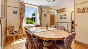A dining room with a wooden table and plaid chairs, a chandelier, and a window with curtains.