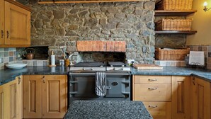 A kitchen with a stone wall, wooden cabinets, a stove, and wicker baskets on shelves.