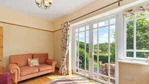 A living room with a sofa, a patterned rug, a large window with a view of greenery, and a chandelier.