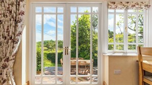 A room with a large sliding glass door leading to a garden, a small window with a floral valance, and a wooden bench.