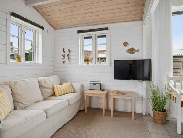 A cozy living room with a white sofa, a flat-screen TV, and a wooden ceiling.