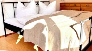 A bed with a beige bedspread, white pillows, and a wooden nightstand with drawers.