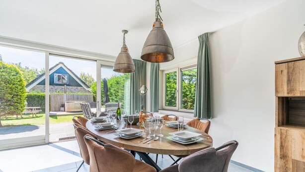 A dining area with a round table set for six, surrounded by six chairs. - Luxury 8-person Holiday Villa (De Koog)