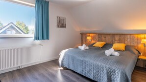 A bedroom with a large bed, a window with curtains, a wooden headboard, and a radiator. - Luxury 8-person Holiday Villa (De Koog)