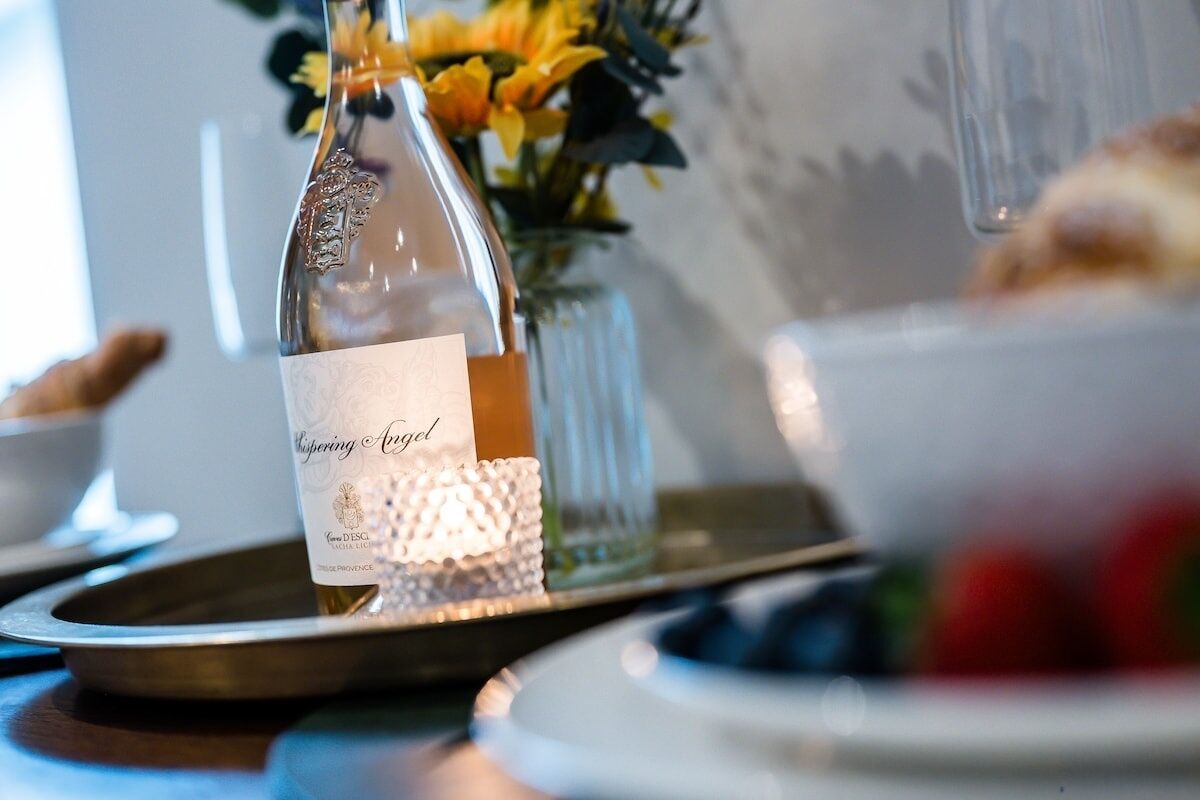Une bouteille de vin, avec son étiquette, posée sur un plateau, accompagnée d’une bougie et d’un vase de fleurs.