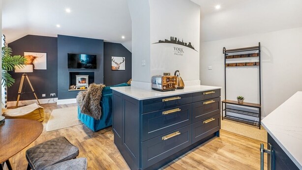 A modern living room with a dark blue cabinet, a flat-screen TV, a fireplace, and a city skyline mural on the wall. - Glasswing Stays | The Holgate Sanctuary (York)