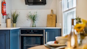 A modern kitchen with a built-in oven, a dishwasher, and a wooden cutting board. - Glasswing Stays | The Holgate Sanctuary (York)