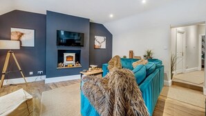 A modern living room with a fireplace, a teal sofa, and artwork on the walls. - Glasswing Stays | The Holgate Sanctuary (York)