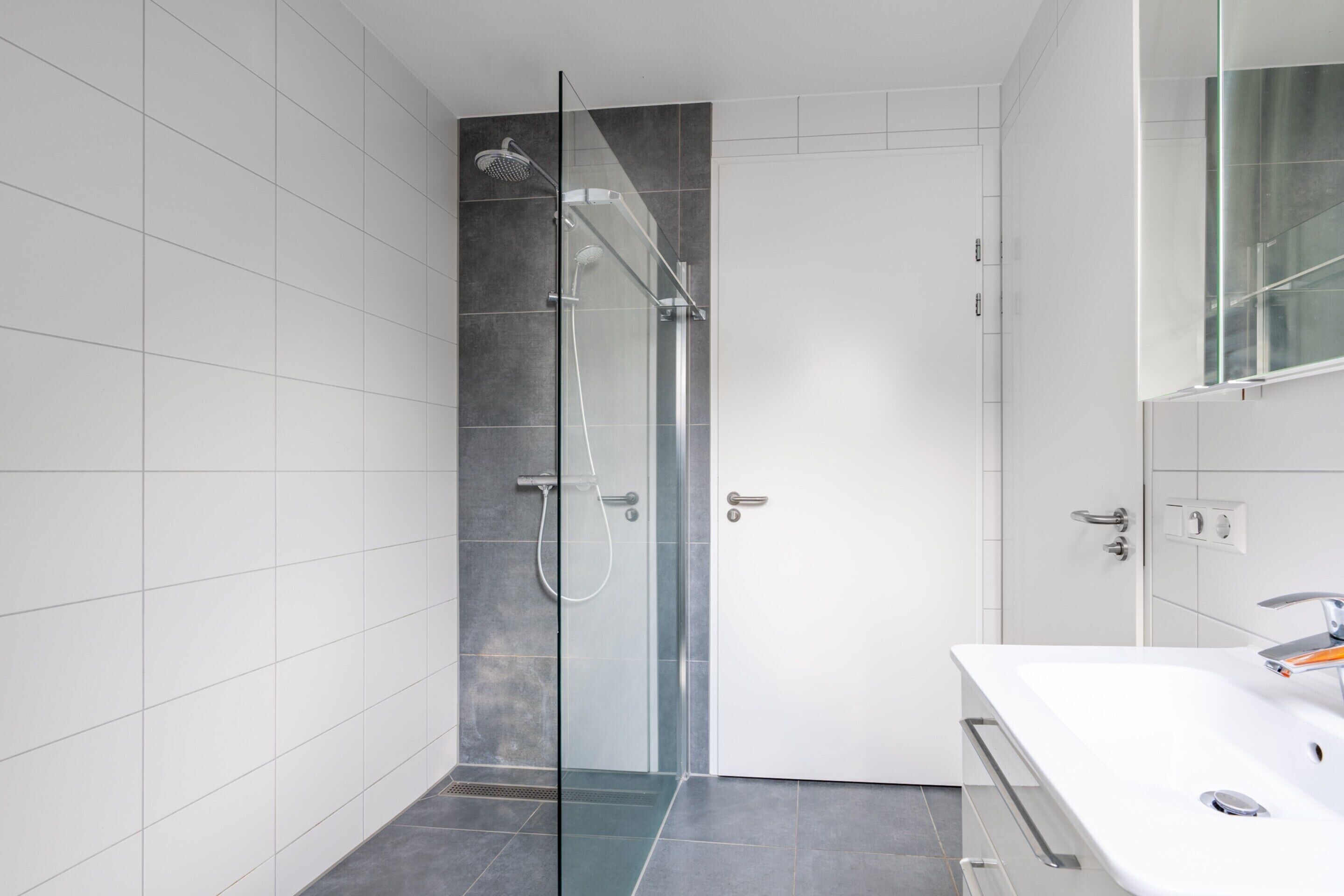 A modern bathroom with a glass-enclosed shower, a white sink, and a large mirror.