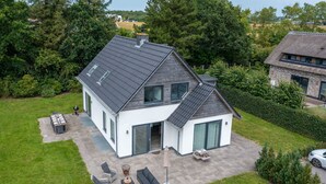 Ein modernes, zweistöckiges Haus mit Satteldach, großen Fenstern und einer Terrasse mit Gartenmöbeln.
