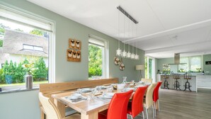 Ein moderner Essbereich mit Holztisch und roten Stühlen, im Hintergrund eine Küche und Blick ins Grüne.
