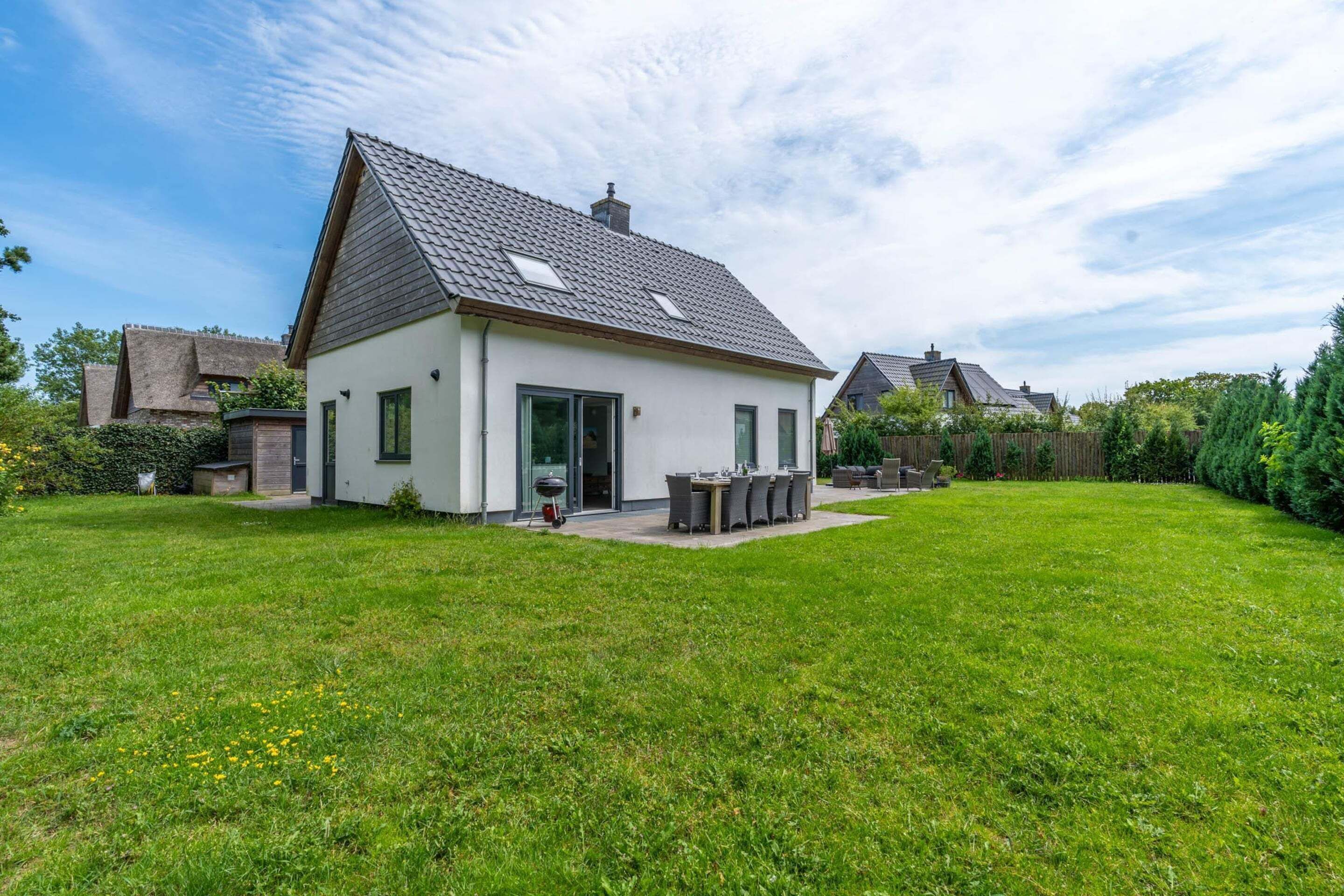 A modern house with a sloped roof, a patio with outdoor furniture, and a well-maintained lawn.
