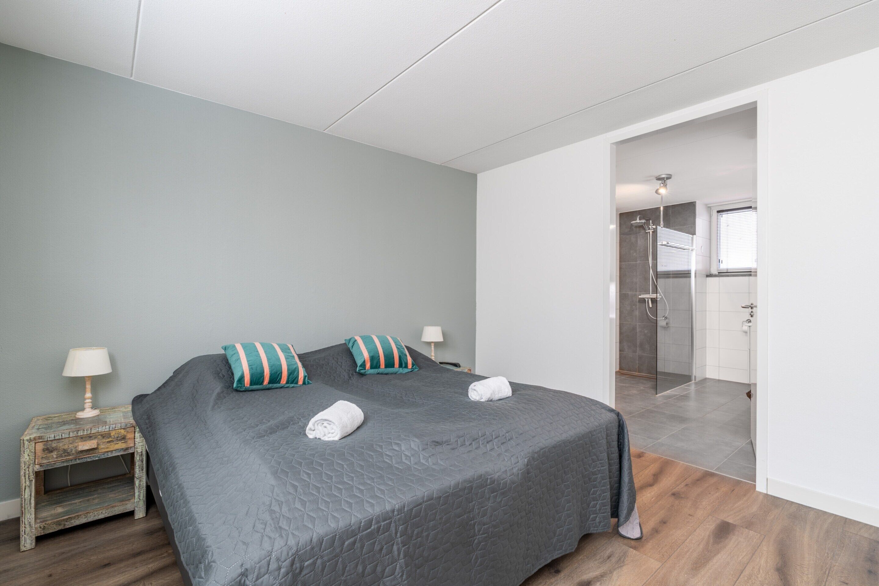 A bedroom with a large bed, a nightstand, a lamp, and a view into the bathroom.