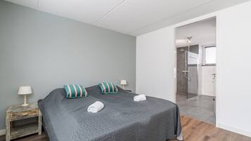 A bedroom with a large bed, a nightstand, a lamp, and a view into the bathroom.