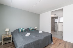 A bedroom with a large bed, a nightstand, a lamp, and a view into the bathroom.