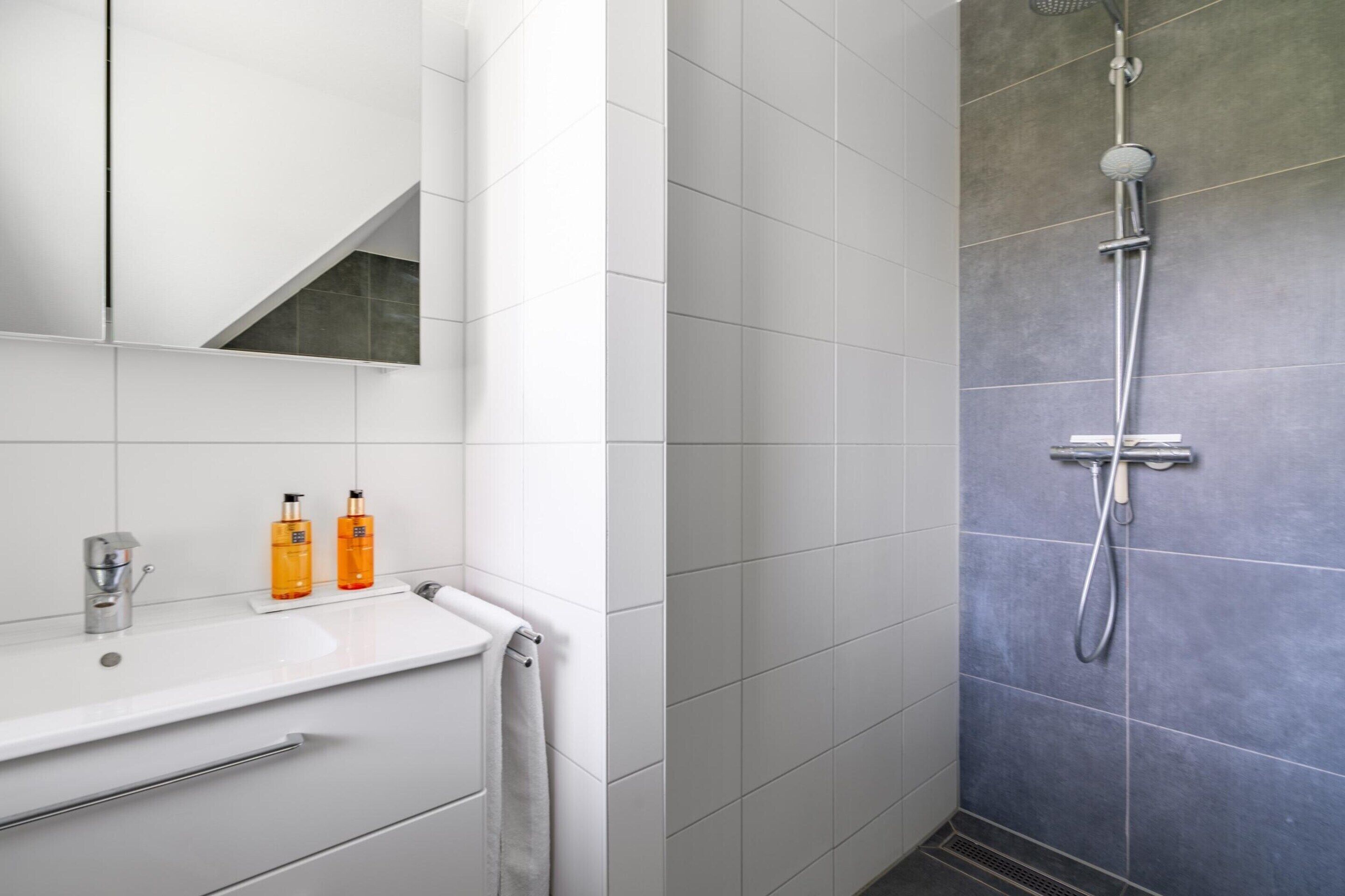 A modern bathroom with a white sink, two orange bottles, a towel, and a shower with a grey wall.