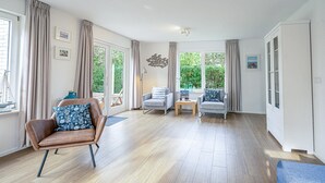Uma sala de estar ampla, com uma poltrona de couro marrom, um sofá cinza e uma pequena mesa de madeira.