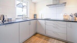 Cozinha moderna com armários brancos, bancada de granito e janela com vista para uma casa.
