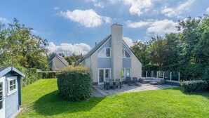 Une maison moderne dotée d’un grand patio, d’un coin repas et d’un petit jardin.