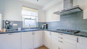 Une cuisine moderne avec des meubles blancs, un plan de travail en granit, une cuisinière à gaz et une fenêtre équipée de stores.