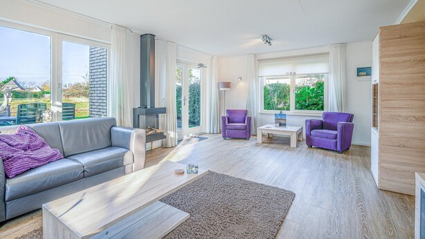 Un salon spacieux avec un canapé gris, deux fauteuils violets, une table basse en bois et une cheminée.