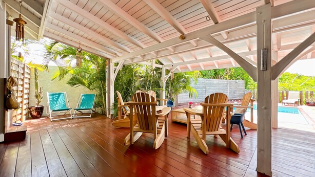 Un espace extérieur abrité, doté de mobilier en bois, d’une piscine et d’une végétation luxuriante.