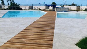 A pool area with two pools, a wooden deck, and a clear sky. - Timoon, 2 bedroom apartment on the beach with amazing view! (Marigot)