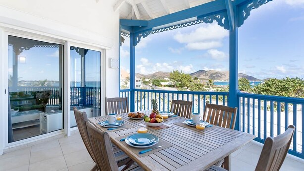 A covered outdoor dining area with a table set for breakfast, overlooking a scenic landscape. - Timoon, 2 bedroom apartment on the beach with amazing view! (Marigot)
