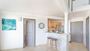 A modern kitchen with a central island, a clock, and a blue floral artwork on the wall. - Timoon, 2 bedroom apartment on the beach with amazing view! (Marigot)