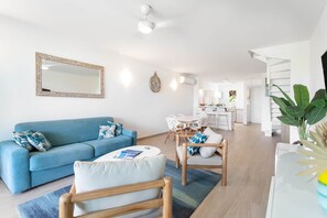 Un salon moderne avec un canapé bleu, des chaises en bois, une table basse et un coin repas doté de meubles blancs.