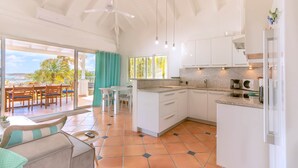A bright kitchen with white cabinets, a dining area with a table and chairs, and a view of the ocean through large windows.