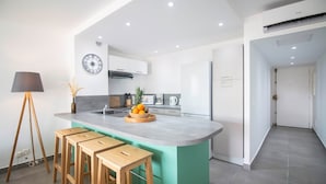 A modern kitchen with a central island, wooden stools, a clock, and a plant. - Blue Wave , charming 2 bedrooms, right behind the beach! (Marigot)