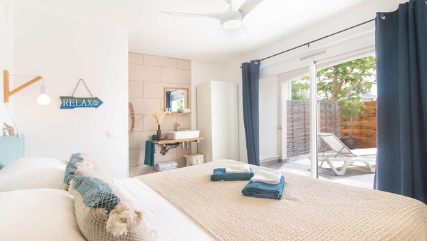 A bedroom with a bed, a bathroom with a sink and mirror, and a sliding glass door to a balcony. - Blue Wave , charming 2 bedrooms, right behind the beach! (Marigot)