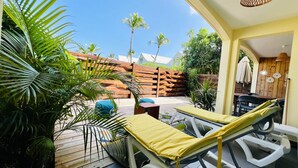 A sunlit patio with lounge chairs, a wooden fence, and tropical plants. - Blue Wave , charming 2 bedrooms, right behind the beach! (Marigot)