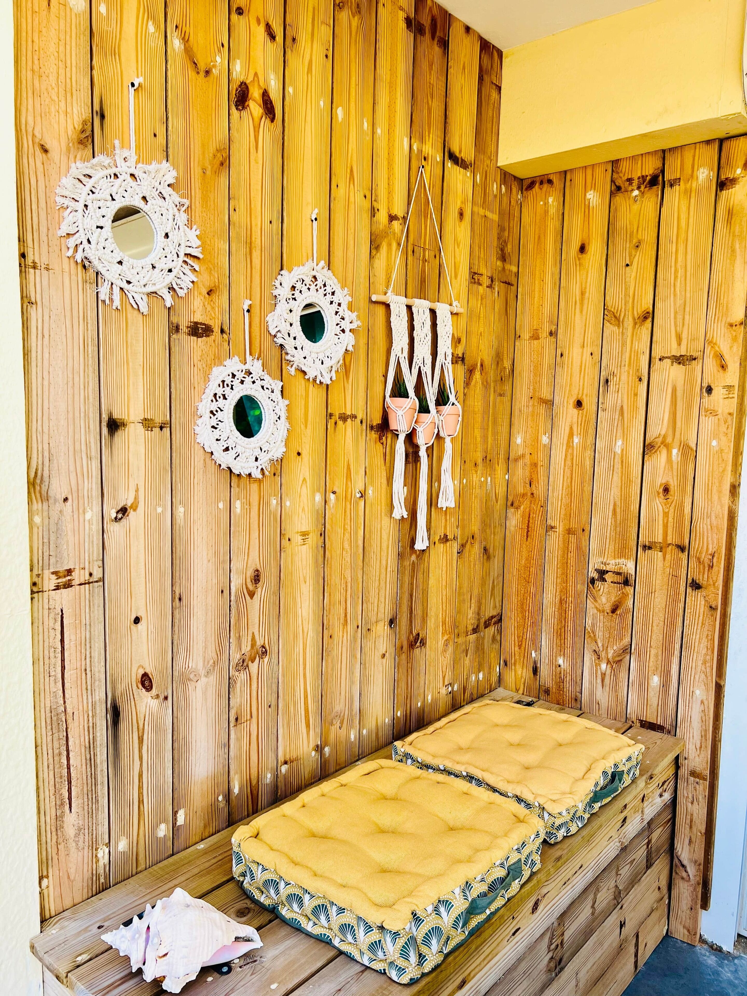 Een kleine, knusse kamer met een houten wand, een bed met een geel dekbed en decoratieve macramé wanddecoraties.