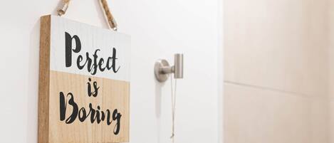 A wooden sign with the text "Perfect is Boring" hanging on a white door.