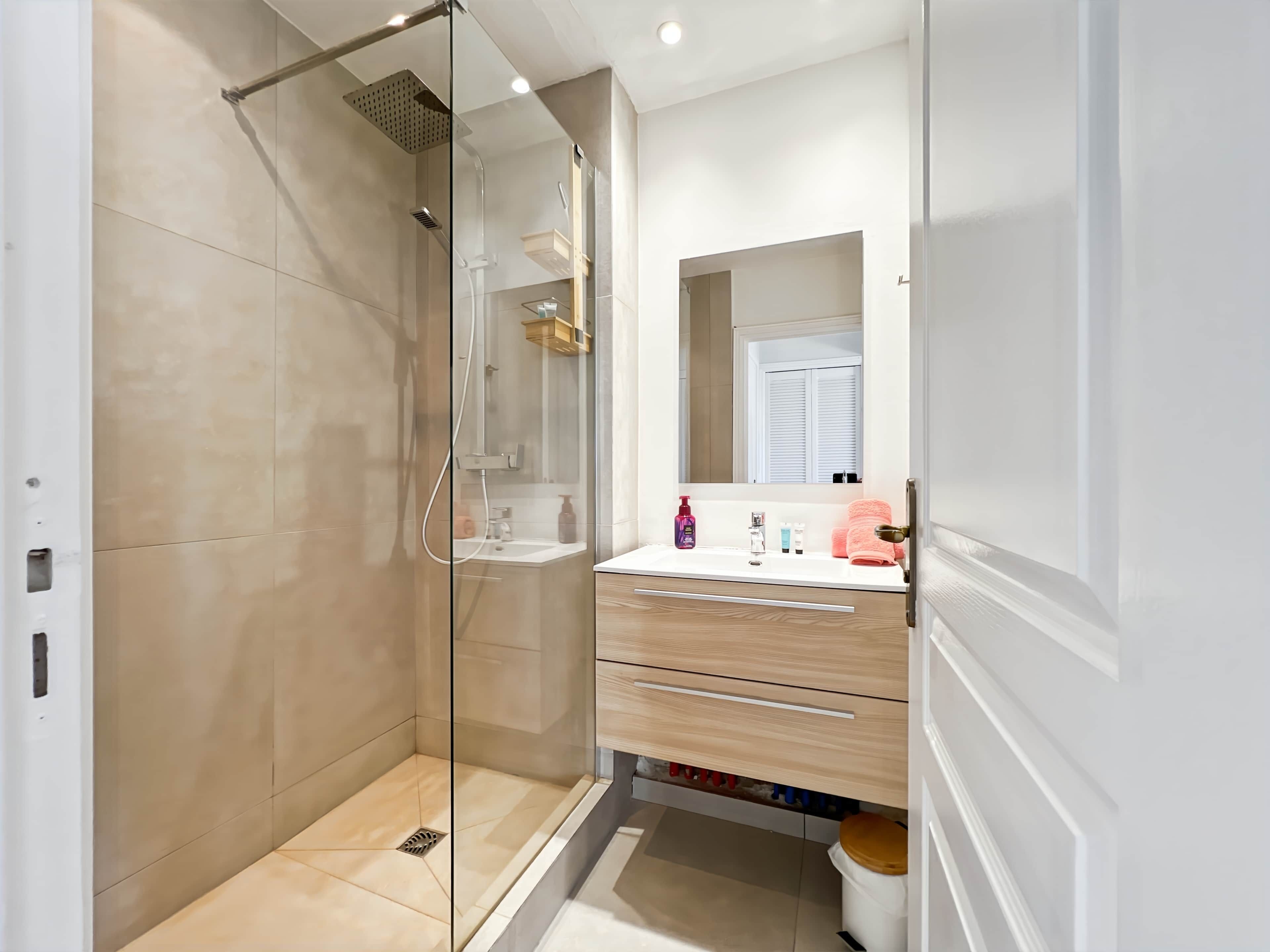 A modern bathroom with a glass-enclosed shower, a white sink with a mirror above, and wooden cabinetry.